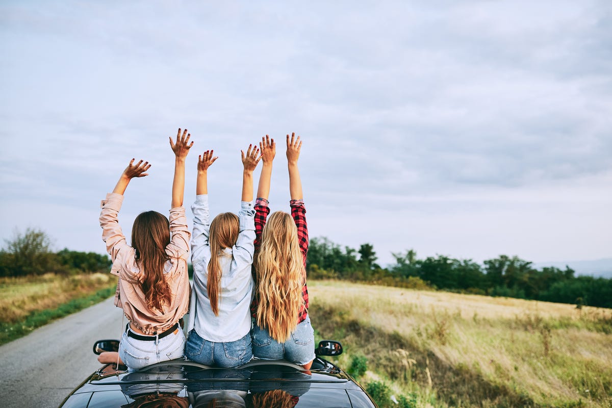 Girlfriends driving on a cabriolet vehicle.