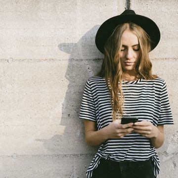 Portrait of fashionable young woman wearing hat using smartphone