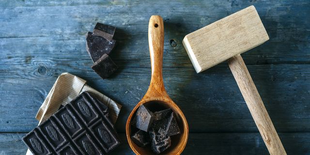 Dark chocolate on paper, wooden spoon and wooden hammer on blue wood