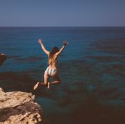 Young woman jumping off cliff and diving into blue sea