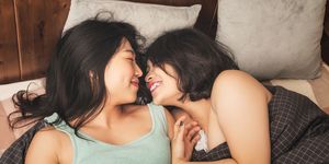 two women laying in bed and cuddling each other while smiling