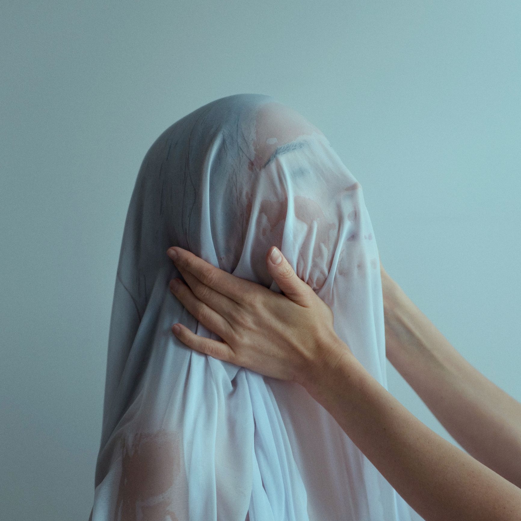 Hands holding head of naked woman covered with wet blue textile
