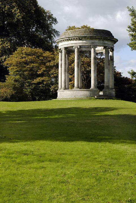 the expansive grounds of an ancestral english country estate with an ornamental rotunda among mature autumn trees in a vertical composition
