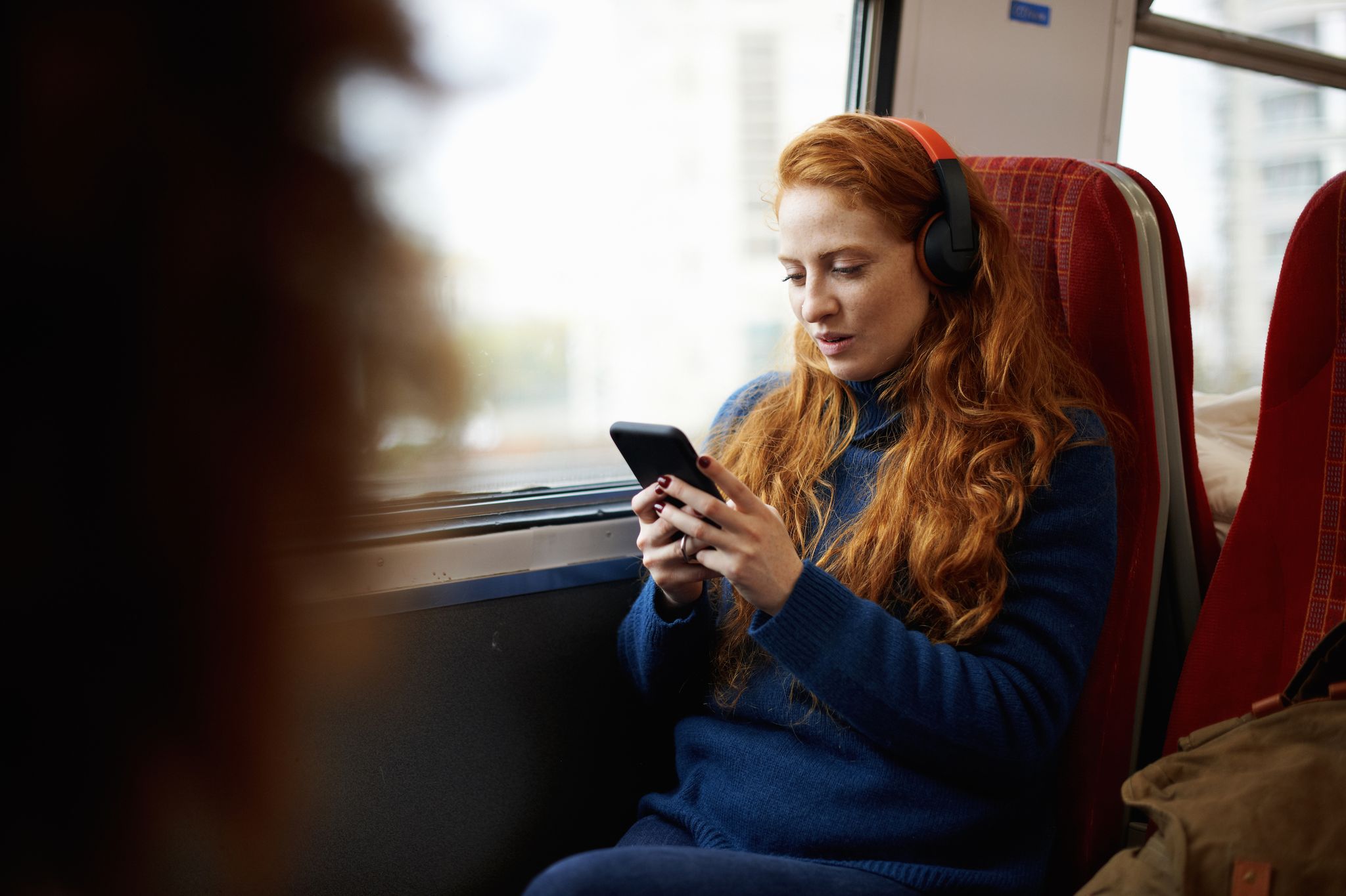Woman on train listening to music on mobile phone with headphones, London