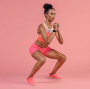sporty woman practicing squat exercises in studio african woman in sportswear working out on pink background