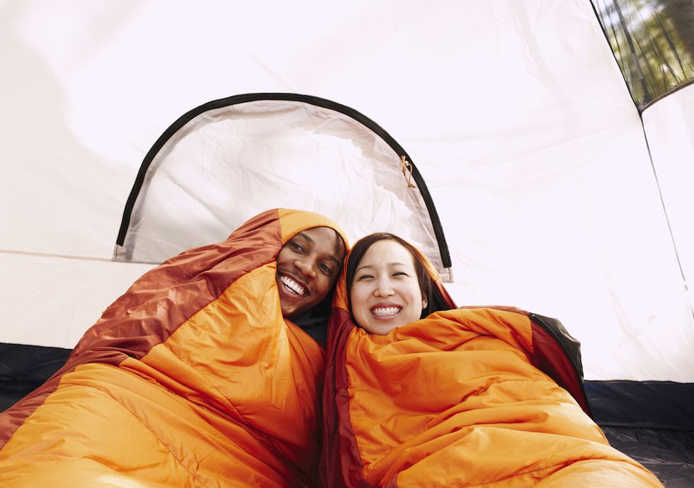 multiethnic couple inside sleeping bags and tent