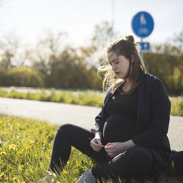 zwangere vrouw zit langs een wandelweg met gesloten ogen