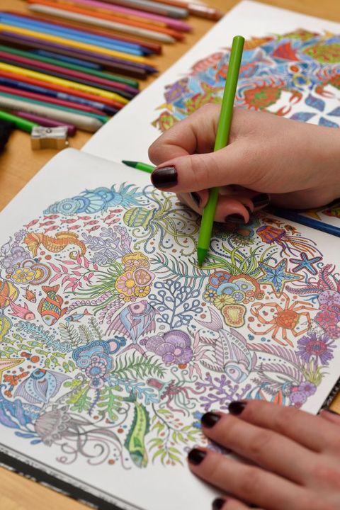 Adult woman with green pencil completing an undersea coloring book on a wood table