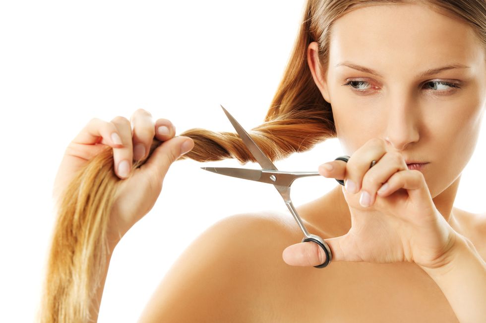 Close-Up Of Woman Cutting Her Hair Against White Background