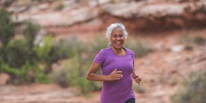 a senior woman goes for a solo run in the utah desert on a sunny afternoon she has a big smile and looks happy as she runs along a trail surrounded by boulders, rocks, sandstone, and sagebrush