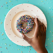 black hand holding donut with sprinkles over plate on blue background