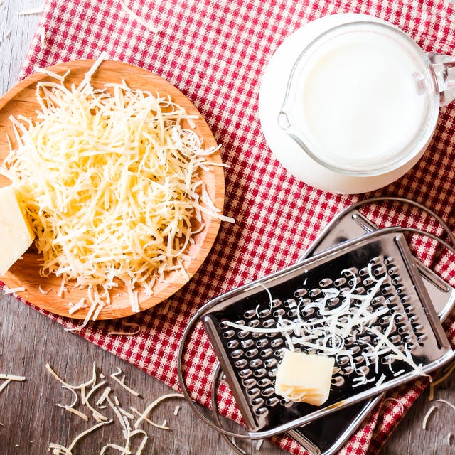 ingredients for pasta dish or pizza milk, freshly grated parmesan cheese on a wooden table, and kitchen utensils (grater) on a wooden table, top view. messy style. preparations for cooking process.