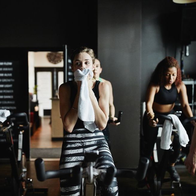 Woman wiping sweat from face with towel during indoor cycling class in fitness studio