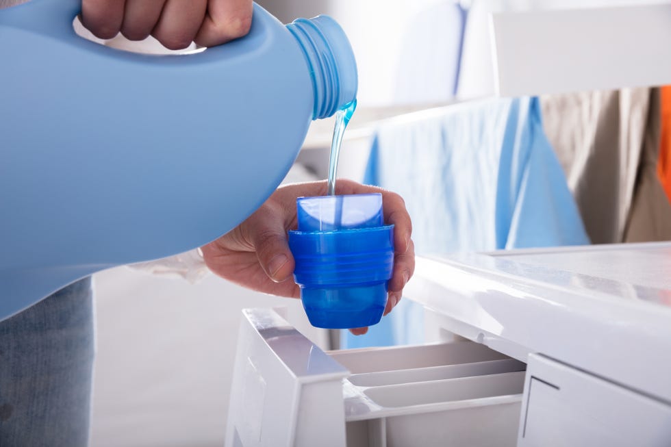 close up of a persons hand pouring detergent in lid