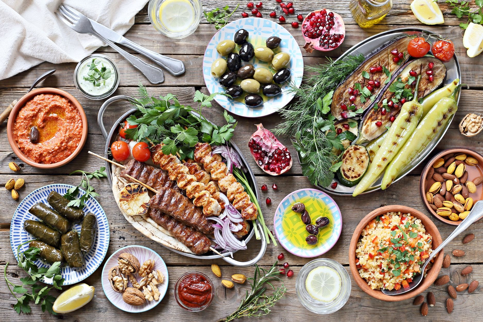 middle eastern, arabic or mediterranean dinner table with grilled lamb kebab, chicken skewers with roasted vegetables and appetizers variety serving on rustic outdoor table overhead view