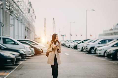 Beautiful young lady using smartphone while walking to car in rooftop carpark in city