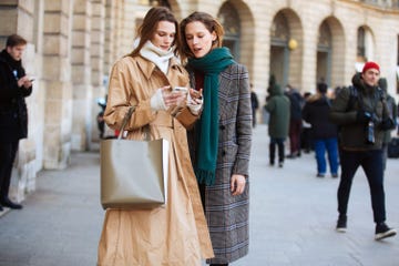 two women interacting while standing on a city street with pedestrians in the background