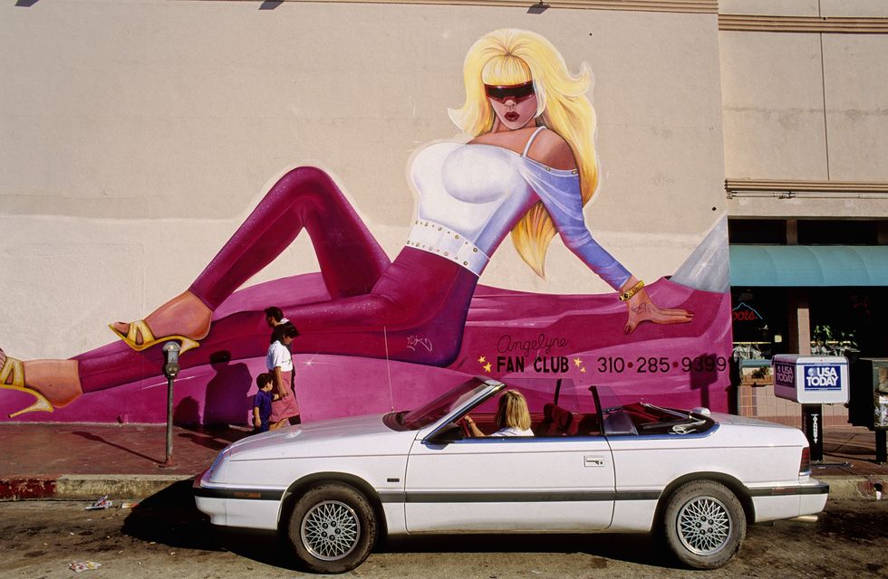 a mural depicting the la pop icon angelyne, with blonde hair, a white top, and pink pants, painted on a wall in hollywood, 2004