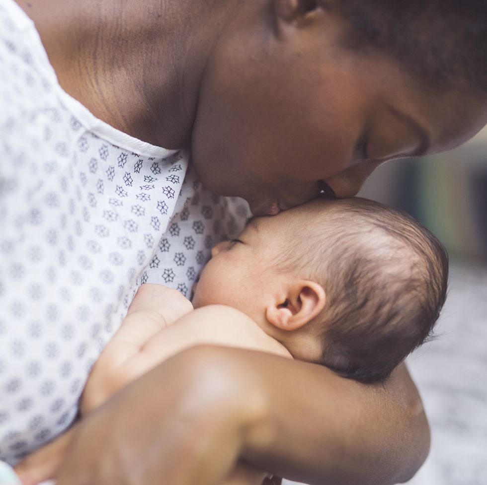a beautiful young african american mother in a hospital gown gently holds her infant in her arms and smiles down at her the babys eyes are closed