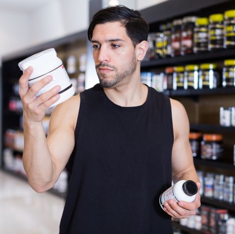 serious muscular guy holding sport nutrition products in sport shop