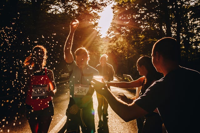 group of athletic people running a marathon at sunset and refreshing with water