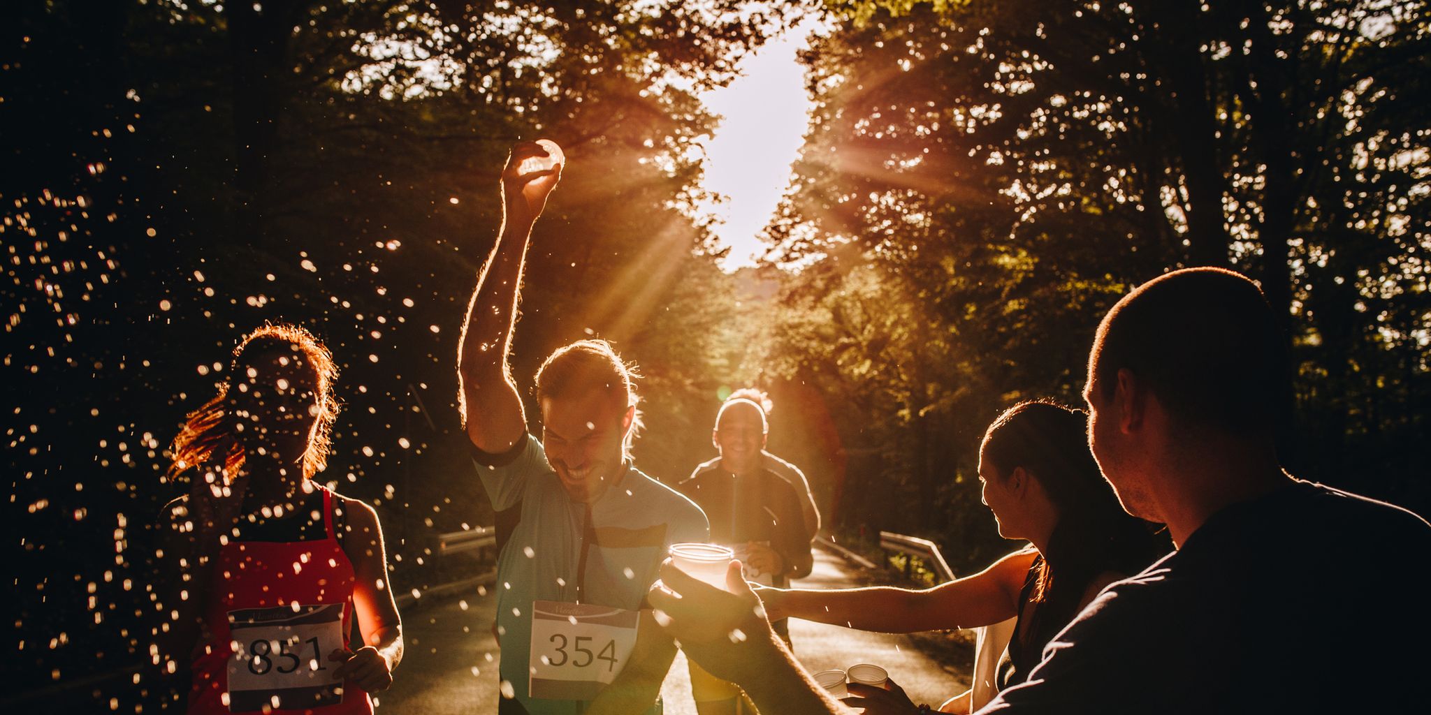 group of athletic people running a marathon at sunset and refreshing with water