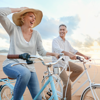 middle age couple riding vintage bicycles on beach at sunset