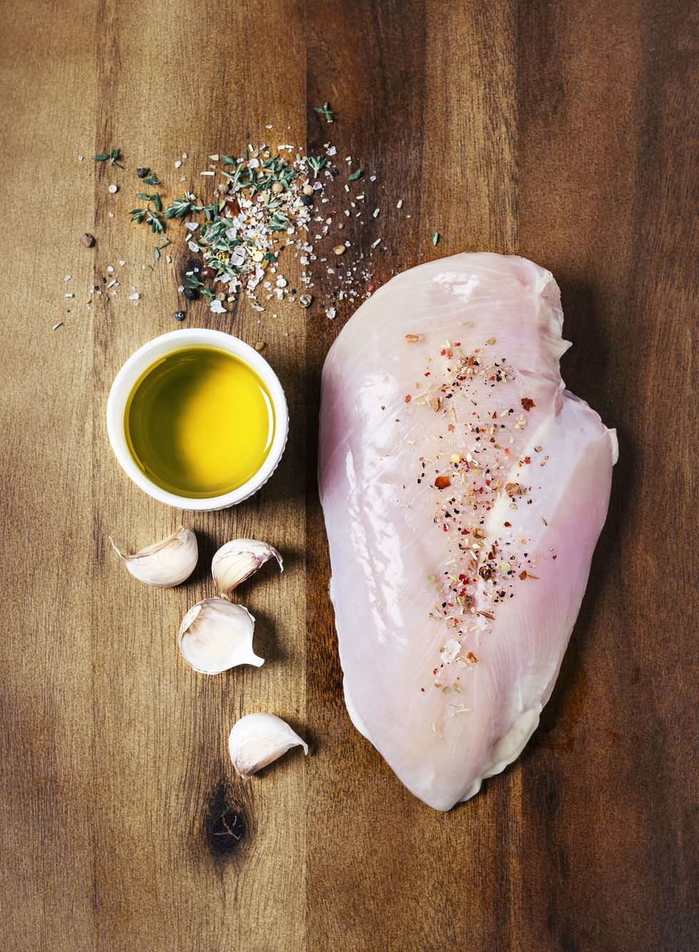 chicken breast with olive oil, garlic, and spices on wooden background