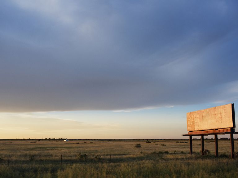 Abandoned billboard on grassy field against cloudy sky