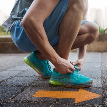 Low section of man tying shoe lace while kneeling by arrow symbol on floor motivazione, voglia di correre