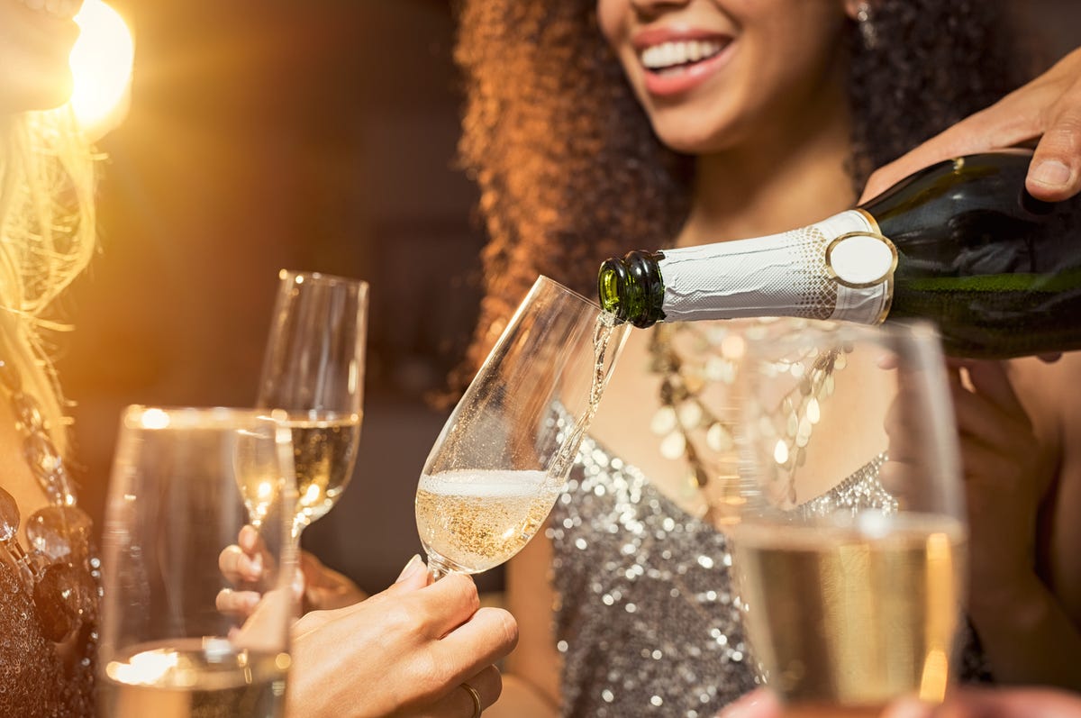 hand pouring champagne from bottle into glasses with friends around him closeup of hand pouring champagne in flutes during new years eve party