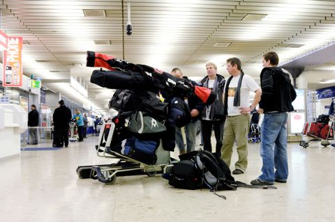 group of men with skis and a baggage trolley in the arrivals concourse of the terminal