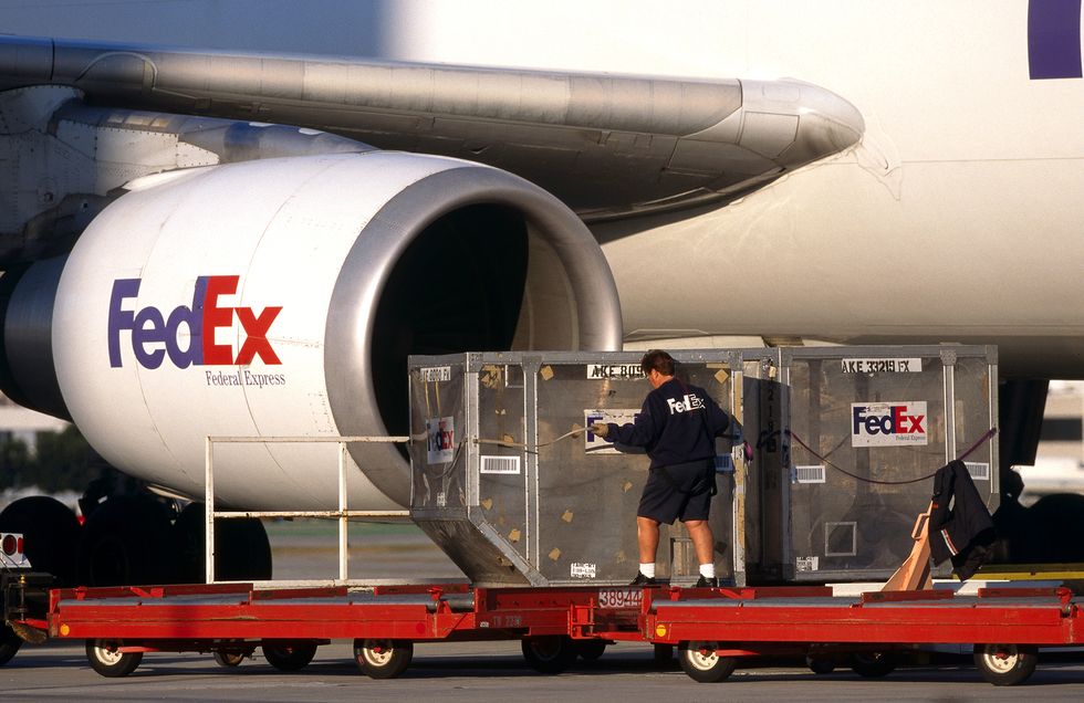 men moving LD3 containers on trolleys with CF6-80 engine-intake of a FedEx Airbus A300-600 freighter