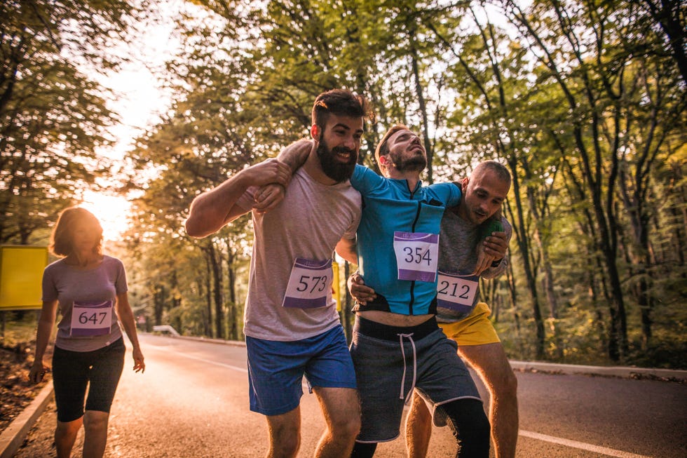 male athletes helping their injured friend during a marathon race on the road through nature