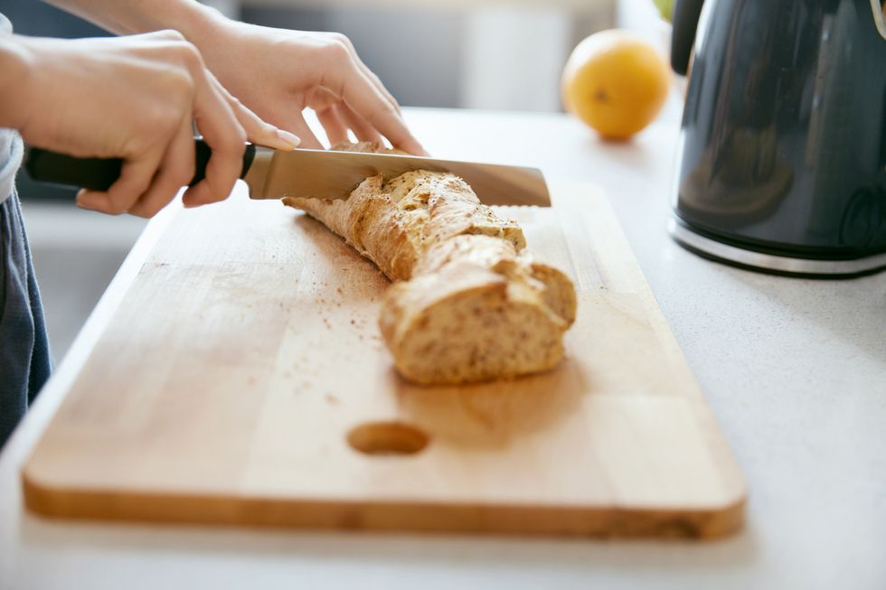 woman hands cutting bread in kitchen close up of female hands holding knife, slicing white baguette on chopping board cooking home high resolution