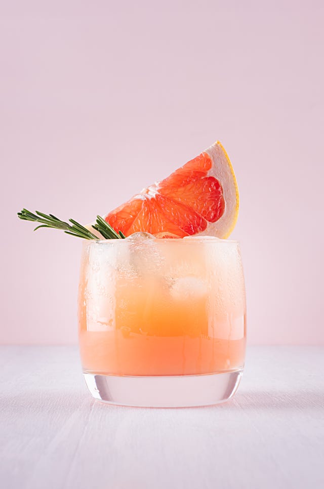 cold detox cocktail of grapefruit juice with ice, rosemary, slices citrus on soft light pink and white background