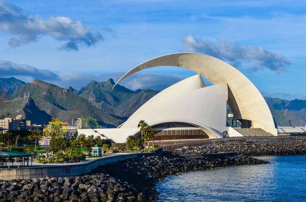 auditorio de tenerife with a curved roof by water and mountains in the background