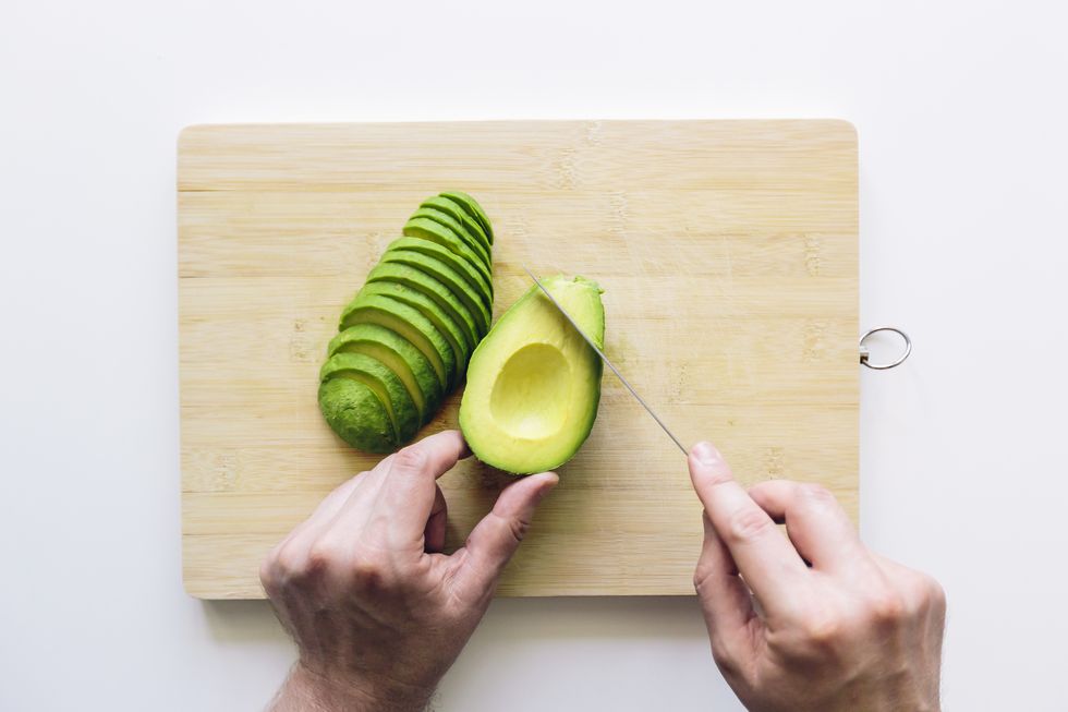man cutting avocado on a wooden cutting board, personal perspective directly above view