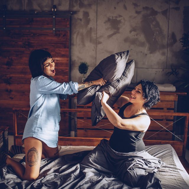 two girls, young lesbian couple relaxing together at home in bed, having a pillow fight