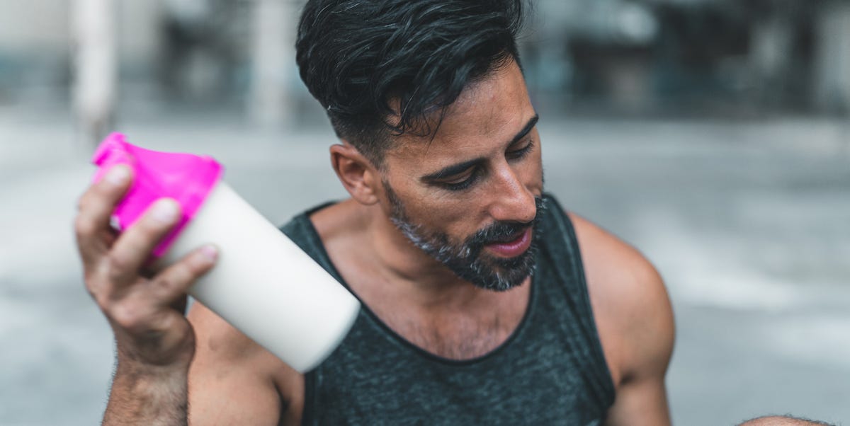 a man is sitting down to mix a protein shake after en exercise inside an abandoned warehouse