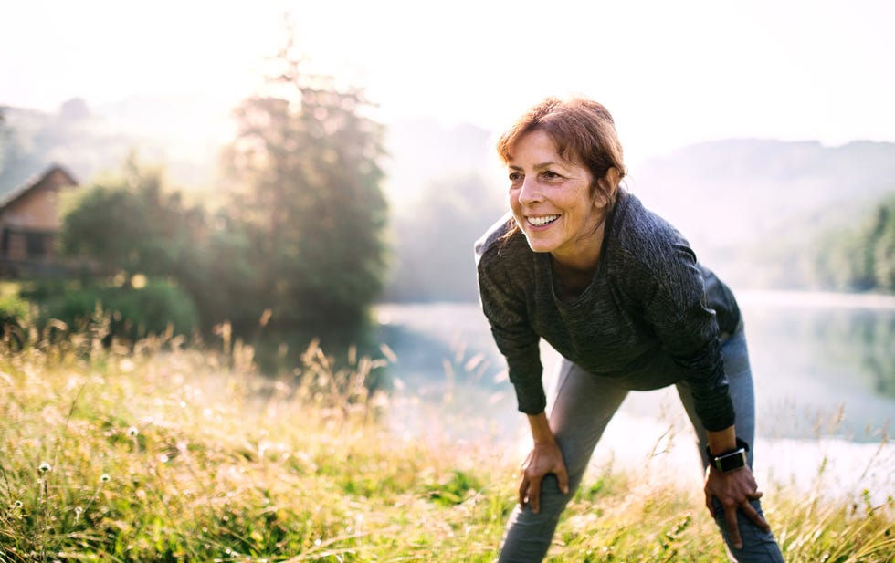 an old female sportsperson dressed in black standing by the lake outside in the countryside