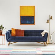 blue and orange painting hanging on a white wall above an elegant sofa with decorative cushions in living room interior real photo