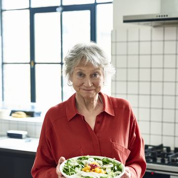 portrait of retired woman in her 60s holding healthy lunch, smiling towards camera in red shirt