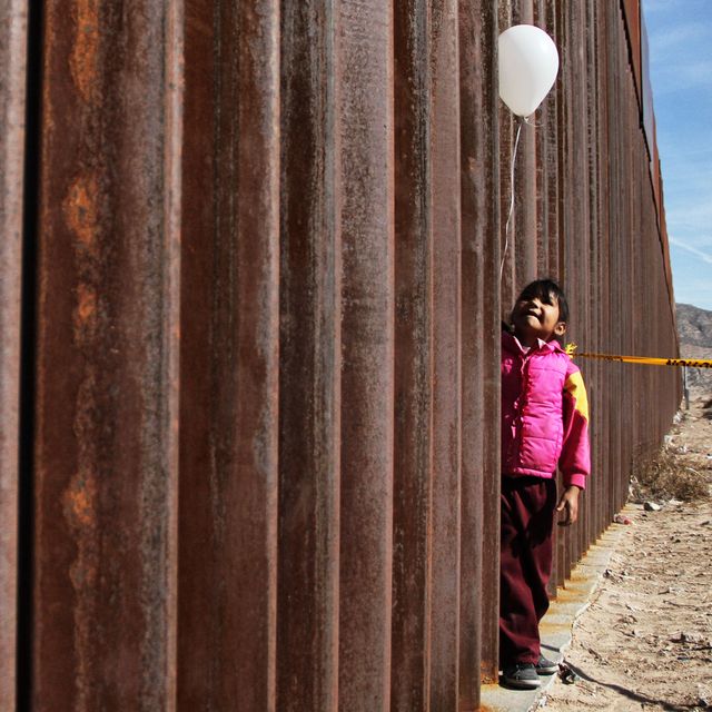 A little girl holds a white ballon at the border wall between Mexico and the United States