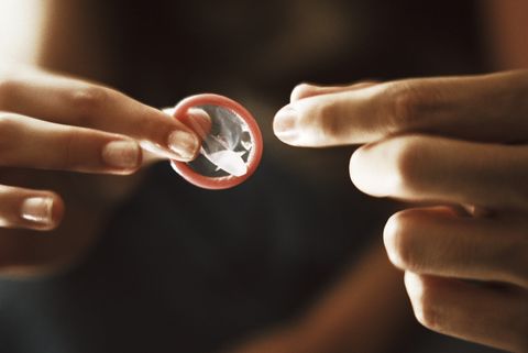 Woman's fingers holding out condom toward man's fingers, close-up