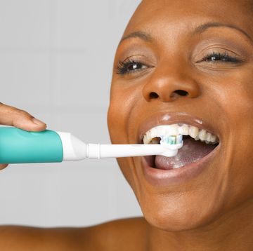 woman lcleaning teeth with electric toothbrush, close up, studio shot
