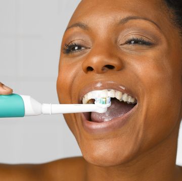 woman lcleaning teeth with electric toothbrush, close up, studio shot
