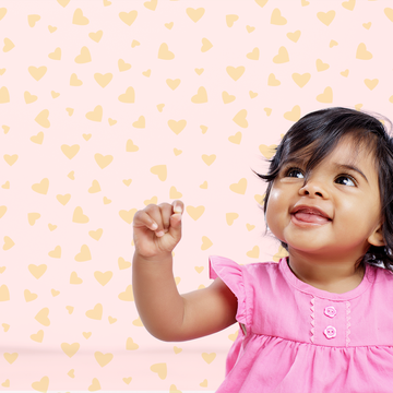 a happy baby girl against a backdrop of hearts on a pink background to illustrate a story about the top baby girl names