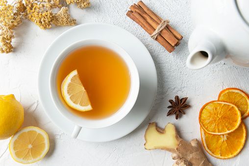 directly above view of a tea cup with herbal tea and a slice of lemon in it surrounded by herbal tea ingredients like chamomile, chamomile tea, lemon, mint leaf, anise, ginger slice, dry orange slices and cinnamon
