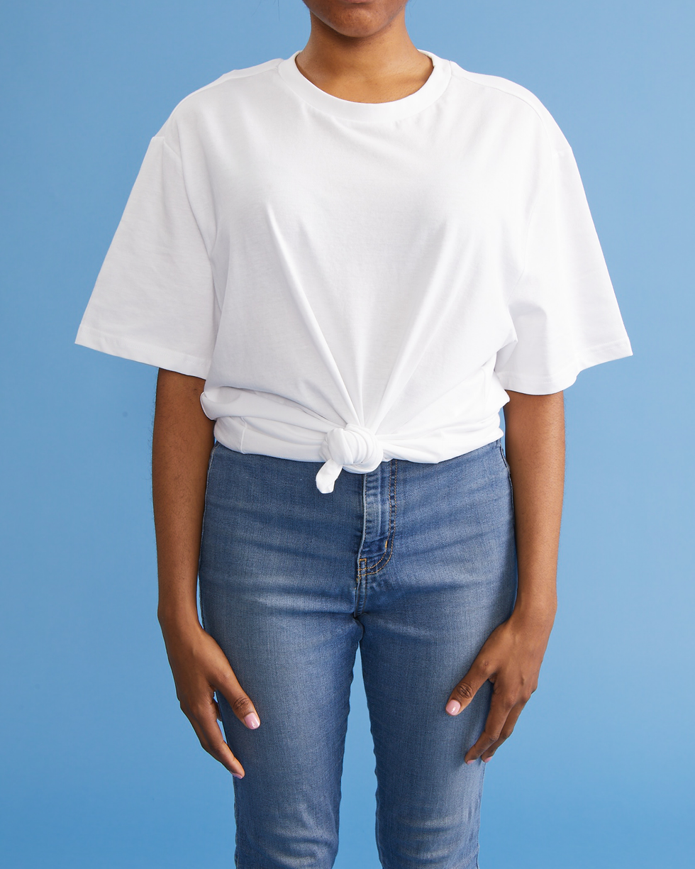 how to tie a shirt front knot, woman standing with hands to her side wearing a plain t and jeans